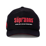 Front-facing image of 'The Sopranos' 25th Anniversary 5-Panel Souvenir Cap with a black base and red lettering in the center saying: "The Sopranos" in the classic Sopranos font, and white lettering saying: "We're just like any other family' directly below that with a red accent on the inside of the brim, all shot on a white background.