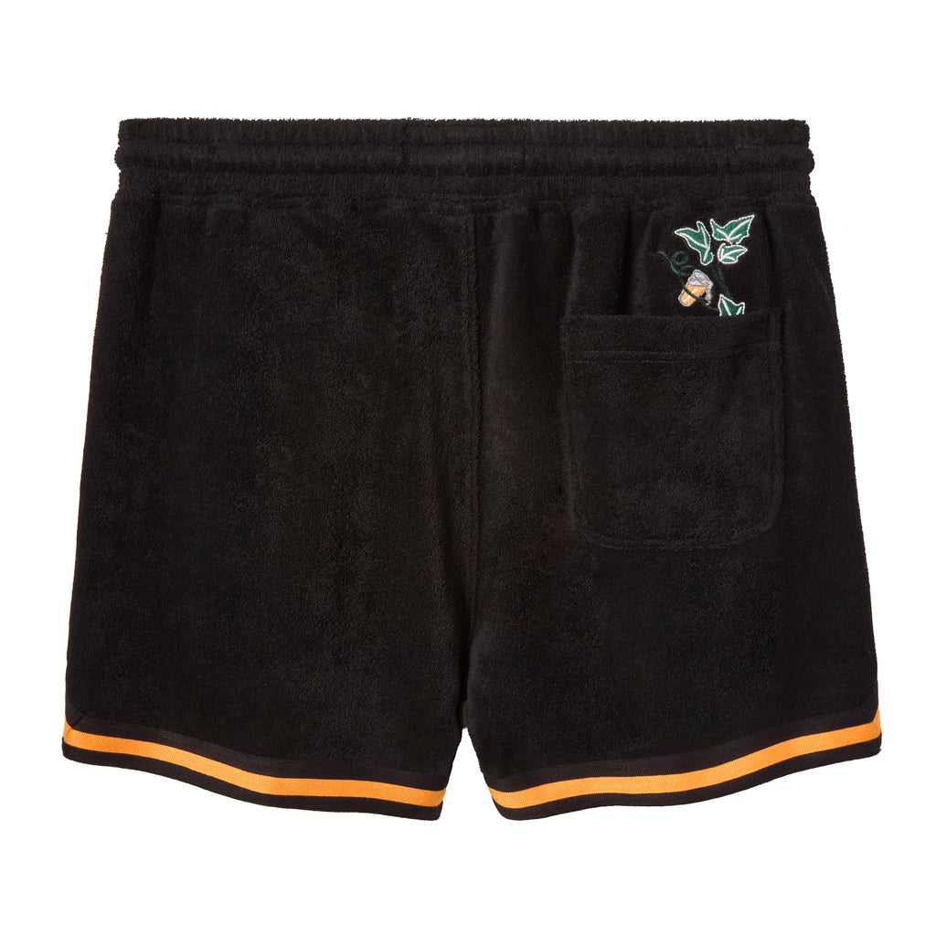 Backside of Black terry cloth shorts with an elastic waistband. Features a back pocket, with greenery and an orange beverage poking out the top.