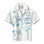 A white short-sleeve shirt with abstract blue embroidery featuring flowers, birds, stars, and faces, with detailed stitching along the edges.
