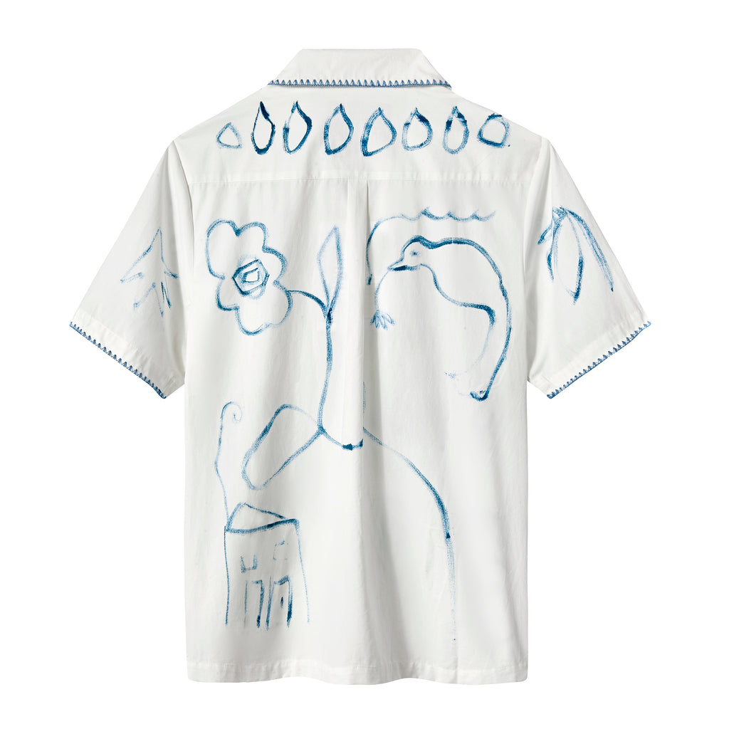 The back of a white short-sleeve shirt featuring abstract blue brushstroke designs of flowers, birds, and leaves, with a row of teardrop shapes across the upper back and stitched trim on the sleeves.
