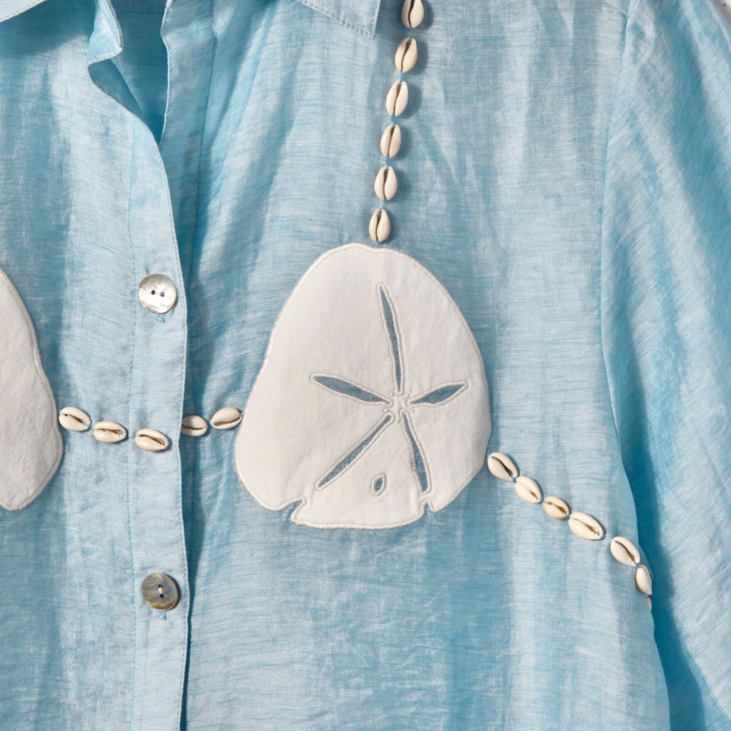 Close-up image of the cream sand dollar details, with cowrie shells replicating bikini strings. 
