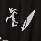 Close-up image of the embroidered surfer, attached to his board with an ankle leash. The ankle leash appears as a small loop to button the shirt.