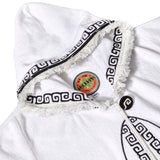 Close-up of white terry cloth hooded beach towel top showing frayed edges, black embroidered trim, and a colorful Tombolo brand label inside the collar.