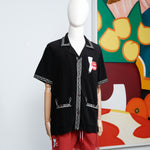 Mannequin dressed in a black embroidered cabana shirt and red swim trunks, both featuring a matching lips and cigarette motif. 