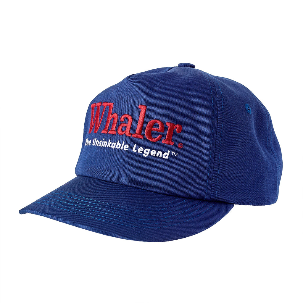 Blue five-panel cap with red embroidered text reading 'Whaler' and white text below reading 'The Unsinkable Legend.' Shown at an angle.