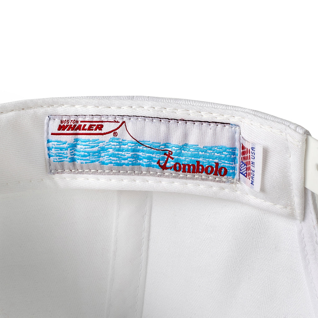 Close-up of the inside label on a white five-panel cap, featuring a Boston Whaler boat graphic above blue waves and red 'Tombolo' text. A 'Made in USA' tag is visible beside it.