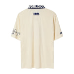 Back view of cream short-sleeve terry cloth zip shirt with navy contrast collar featuring white lettering, small FIFA World Cup 2026 logo centered below the collar, and embroidered skyline graphics on the sleeves.