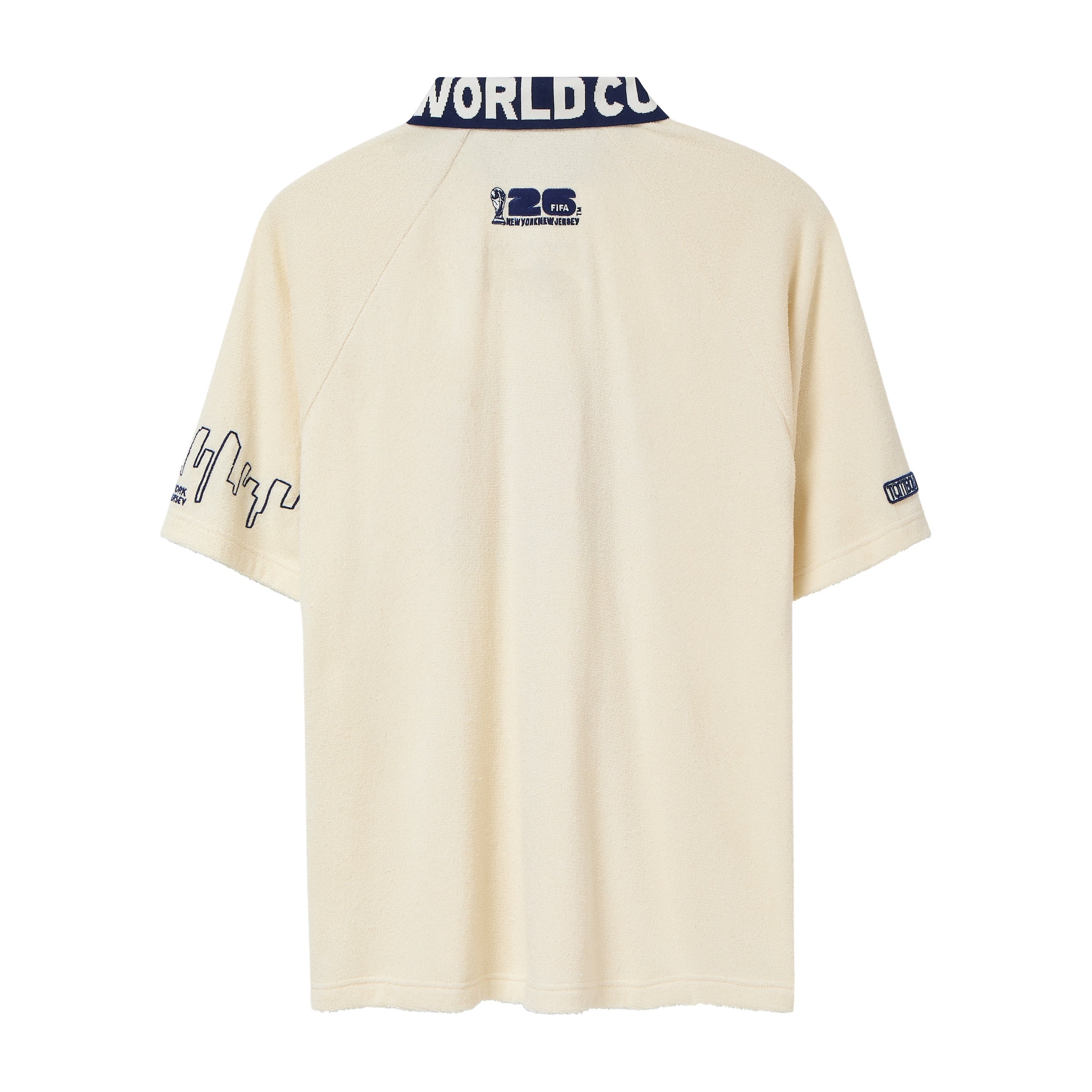 Back view of cream short-sleeve terry cloth zip shirt with navy contrast collar featuring white lettering, small FIFA World Cup 2026 logo centered below the collar, and embroidered skyline graphics on the sleeves.