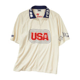 Cream short-sleeve terry cloth zip-front shirt with large red “USA” appliqué across the chest, navy contrast collar with white lettering, and embroidered skyline graphics on the sleeves.