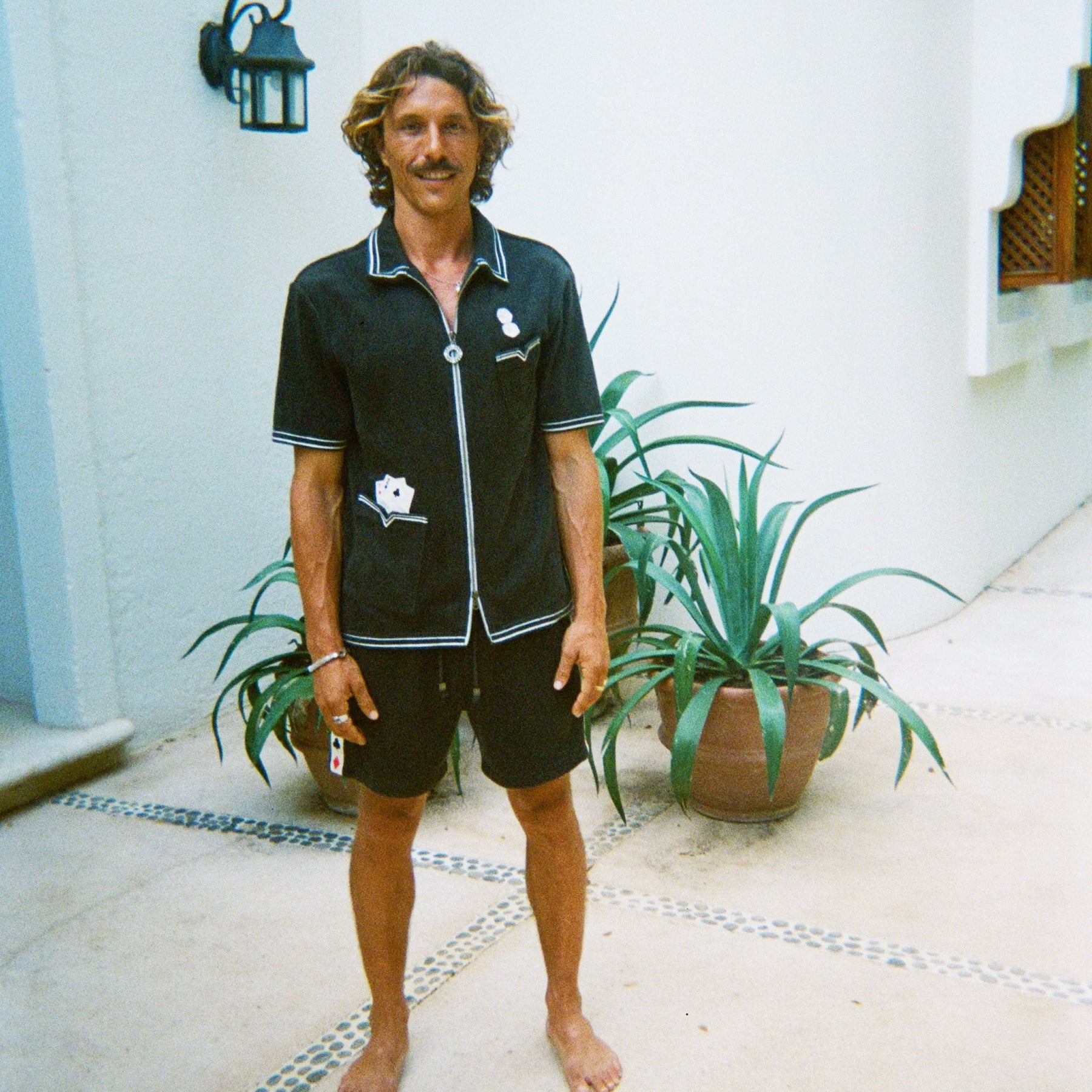 Male model standing and smiling, wearing dark green gambling themed terry cloth cabana, with matching shorts and no shoes. 