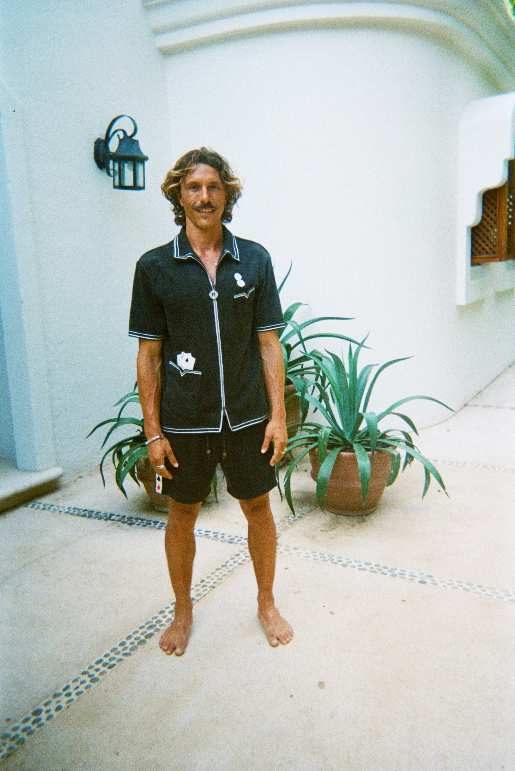 Male model standing and smiling, wearing dark green gambling themed terry cloth cabana, with matching shorts and no shoes. 
