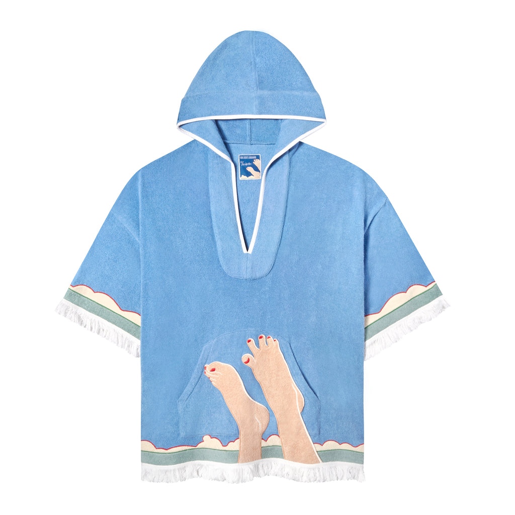 Tombolo blue poncho with embroidered feet in front of seascape