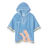 Sky blue terrycloth poncho with white fringe and trim, featuring an embroidered design of legs with red-painted toenails and waves along the hem. 'Tombolo' is stitched in white on the chest.