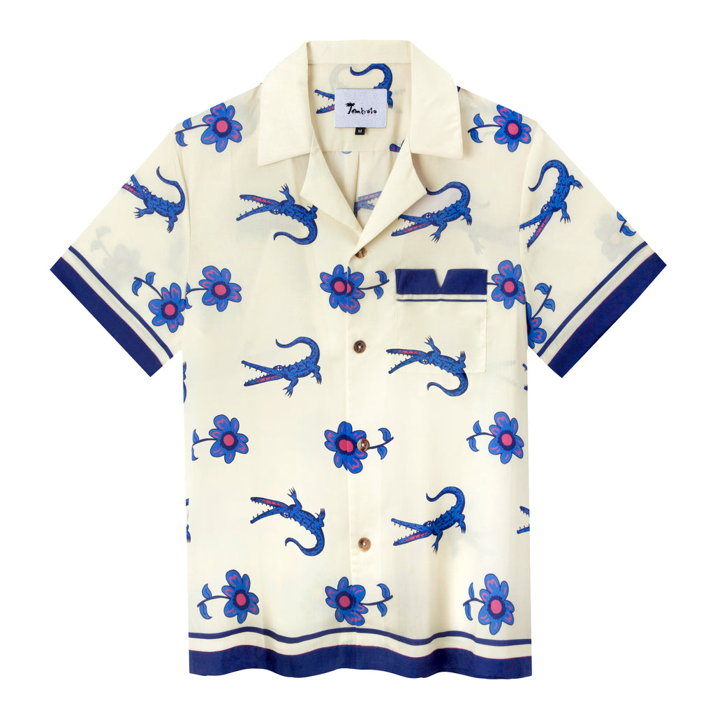 Cream-colored shirt with repeating pattern of crocs and flowers featuring dark blue contrasts on the pockets and the sleeves, along with four brown buttons down the front