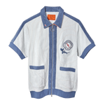 Short-sleeved zip-up terry cloth shirt in white with blue trim and piping. Features two front pockets, a ring zipper pull, and a chest patch with “The Explorers Club NYC,” the letters “E” and “C,” and a small shark illustration.