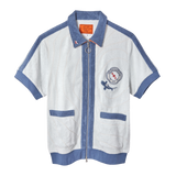 Short-sleeved zip-up terry cloth shirt in white with blue trim and piping. Features two front pockets, a ring zipper pull, and a chest patch with “The Explorers Club NYC,” the letters “E” and “C,” and a small shark illustration.