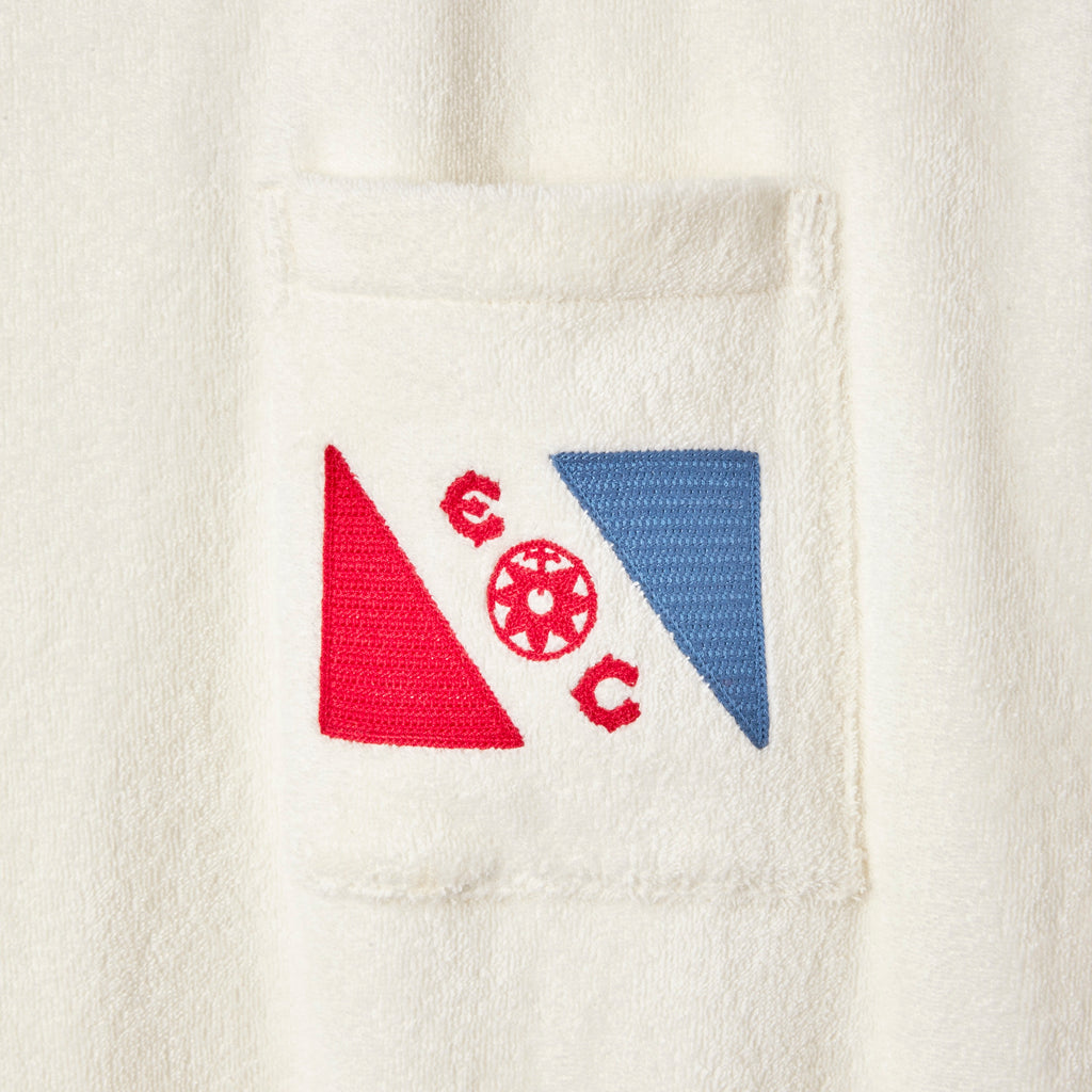 Close-up of a cream terry cloth pocket with an embroidered design featuring a red triangle, a blue triangle, and a central ship wheel surrounded by the letters “E,” and “C” in red.