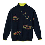 Navy blue knit sweater with neon yellow and red embroidered fish and lettering. Features labeled fish including “Striped Bass,” “Atlantic Cod,” “Sardines,” and a large “Great White Shark” with the word “Human” inside. Neon yellow accents line the collar, cuffs, and hem.