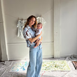 Mary Ball standing in her studio with her baby in her arms and smiling at the camera. 