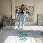 Mary Ball tying her hair back and looking down at her painting in her studio.