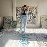 Mary Ball tying her hair back and looking down at her painting in her studio.