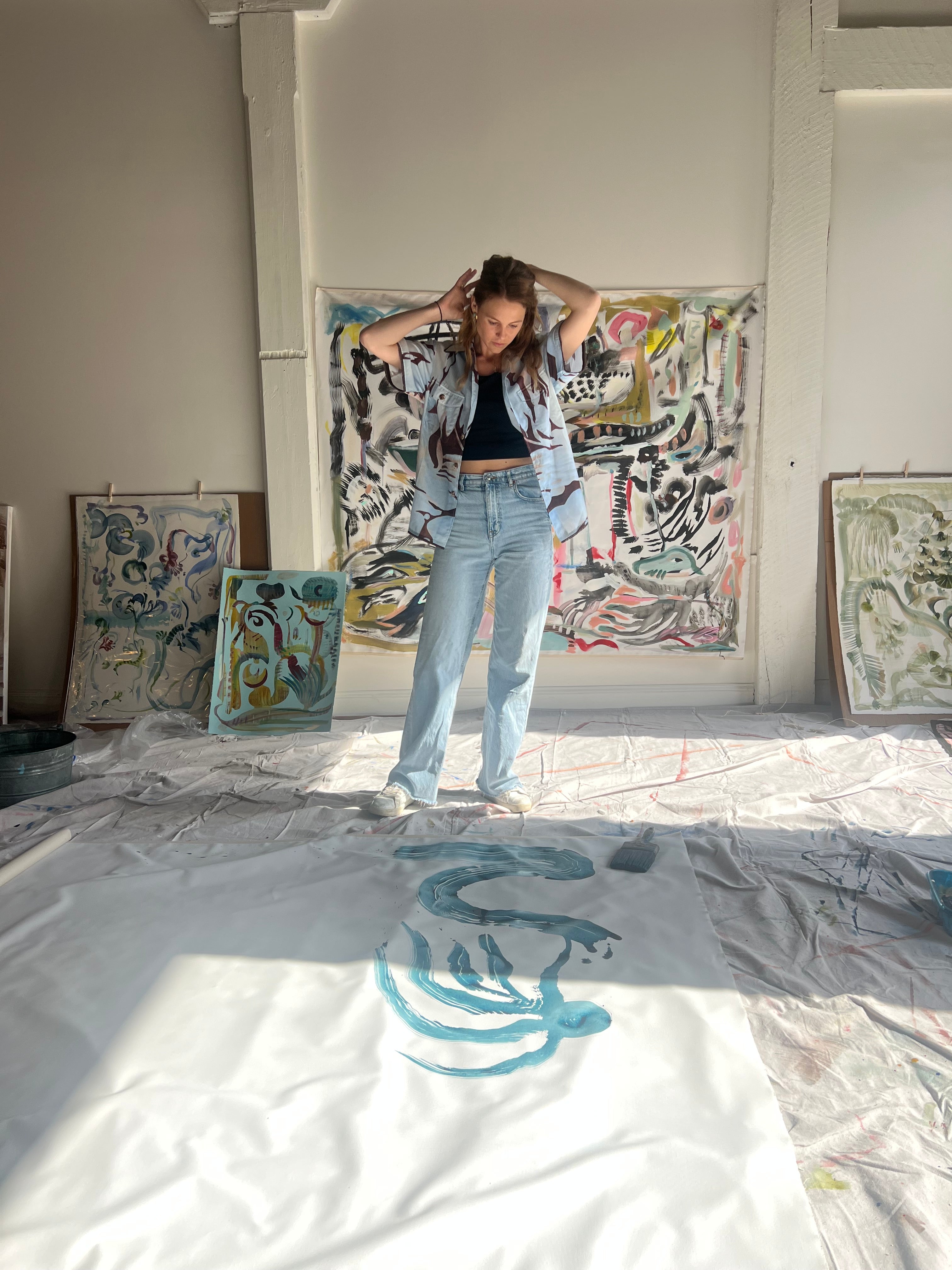 Mary Ball tying her hair back and looking down at her painting in her studio.