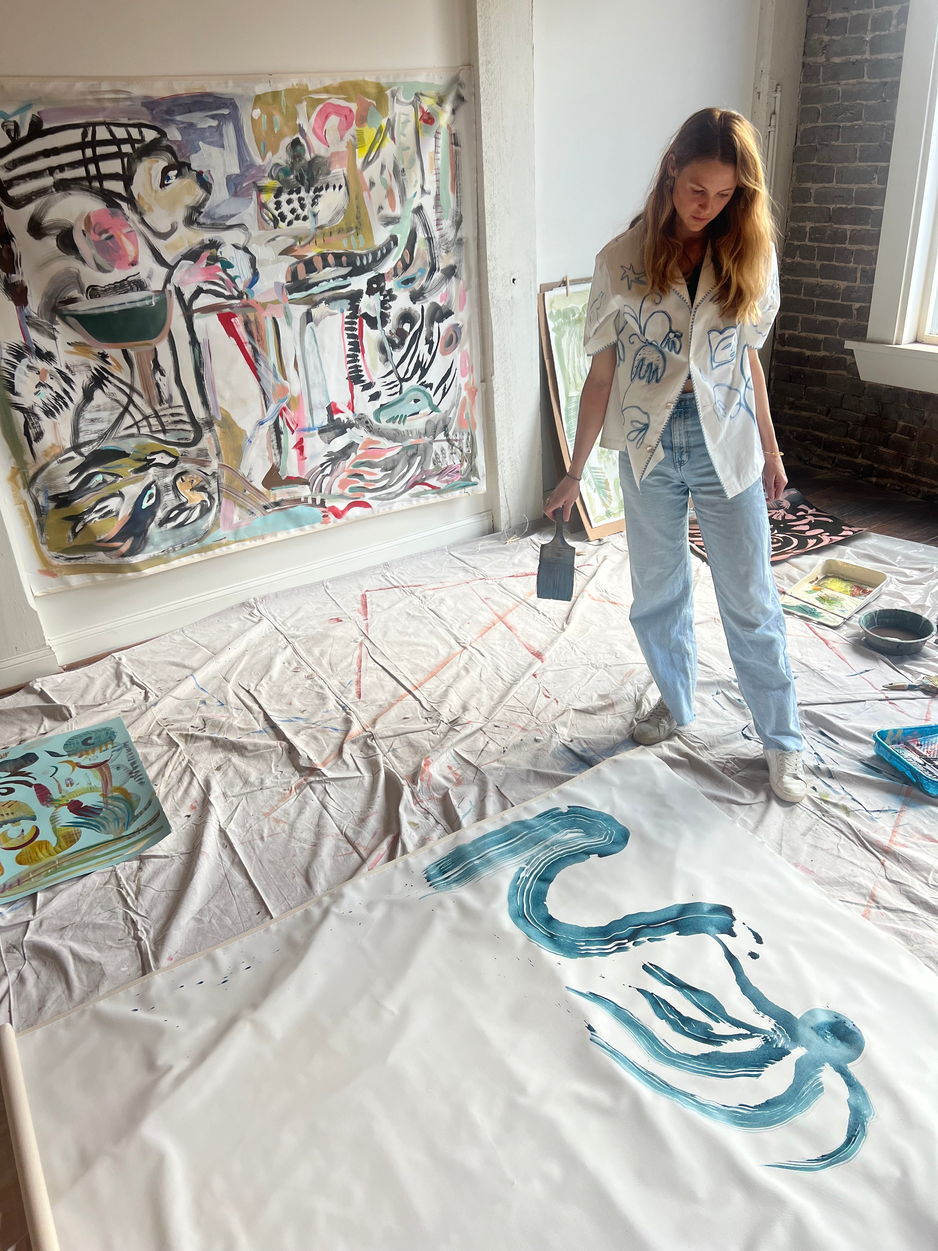 Mary Ball wearing her 'Seasons of Change' Shirt in her studio, looking down at some of her paint strokes. 