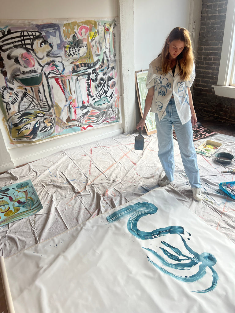 Mary Ball wearing her 'Seasons of Change' Shirt in her studio, looking down at some of her paint strokes. 