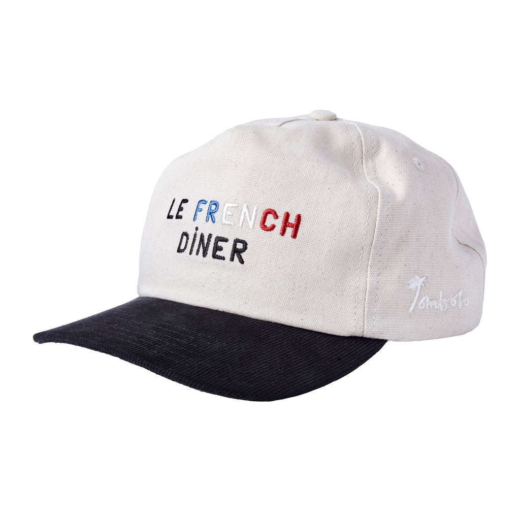 A beige canvas baseball cap with a black brim, shown from a side angle. The front is embroidered with the words “LE FRENCH DINER,” and the side features a small white embroidered 'Tombolo' logo.