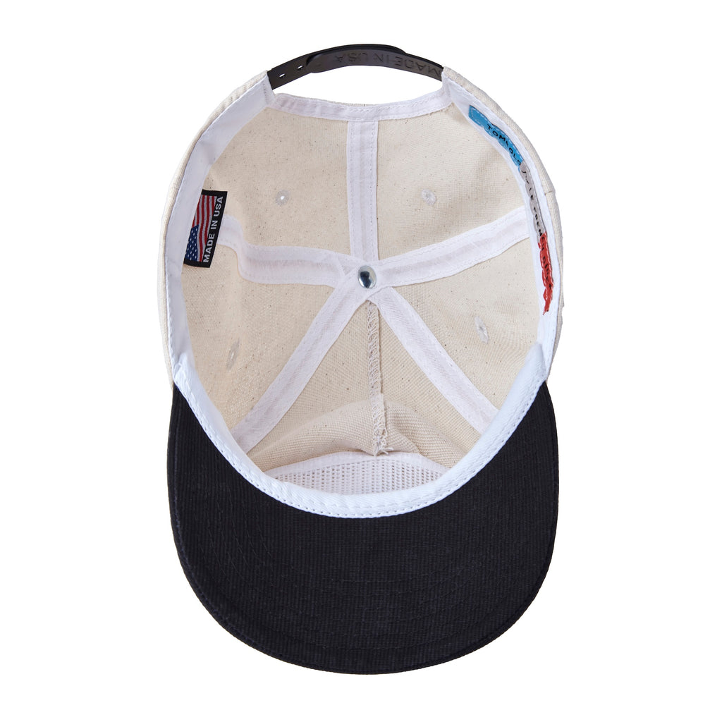 Inside view of a beige canvas baseball cap with a black brim. The interior shows white stitched panels, a “Made in USA” tag, and a colorful label reading “Tombolo for Le French Diner.”