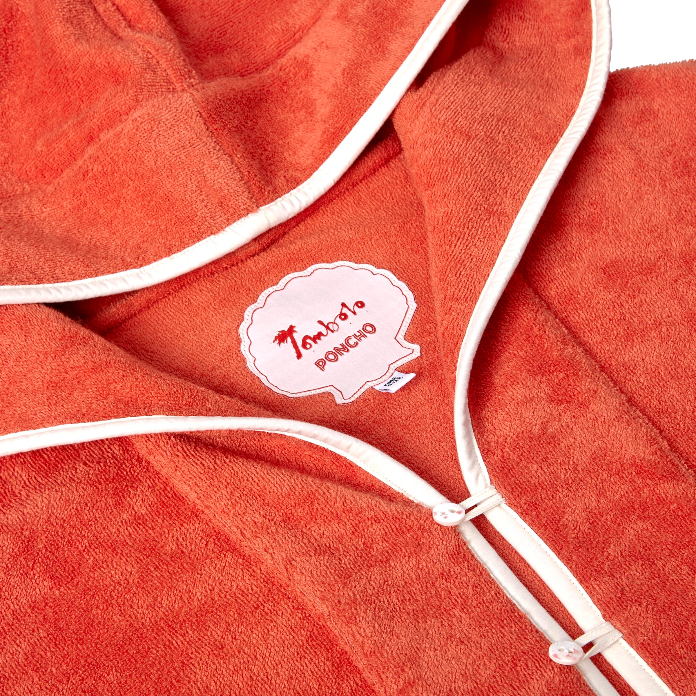 Close-up product image of the 'Scallop' Beach Towel Top's custom woven interior label saying 'Tombolo Poncho,' in addition to the two button and loop closures on collar opening