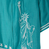 Close-up of white embroidered Statue of Liberty embroidery on teal cabana shirt, stitched along the front panel near the zipper.