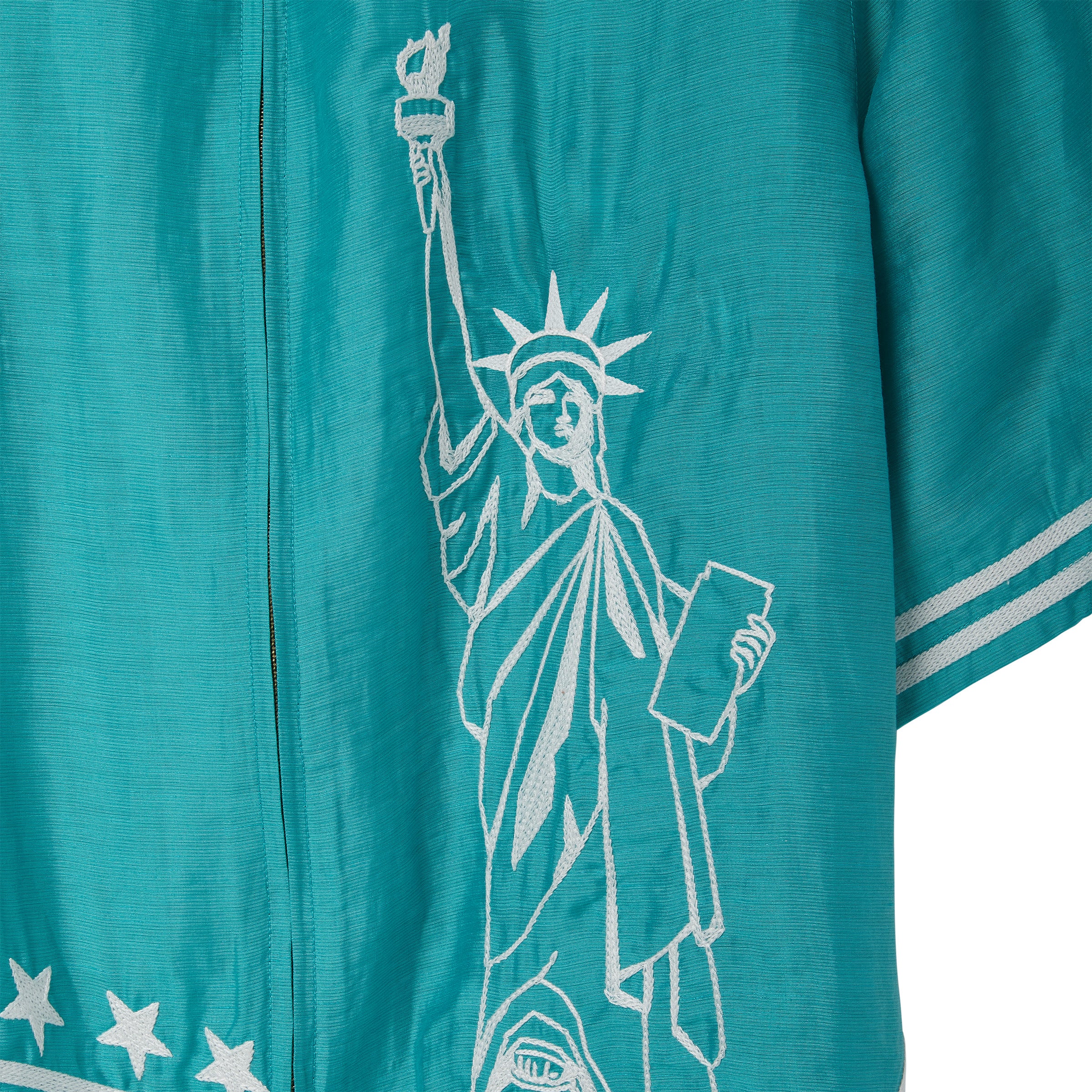 Close-up of white embroidered Statue of Liberty embroidery on teal cabana shirt, stitched along the front panel near the zipper.