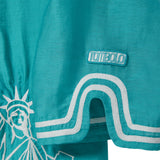 Teal blue shirt with white embroidery and white 'Tombolo' logo patch.