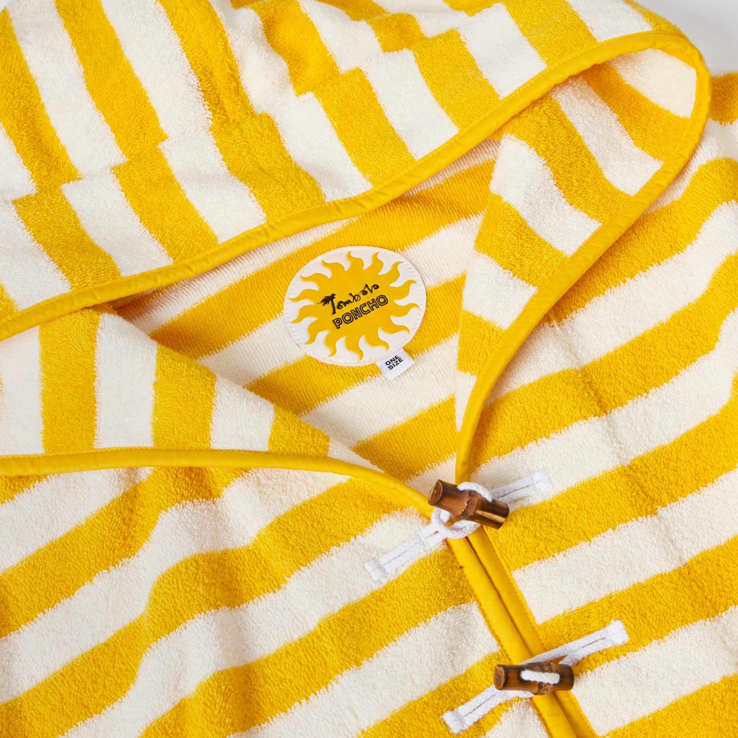 Close-up product image of the 'Saffron Stripe' beach towel top's circular interior tag with sun pattern and bamboo toggles and loop holds.