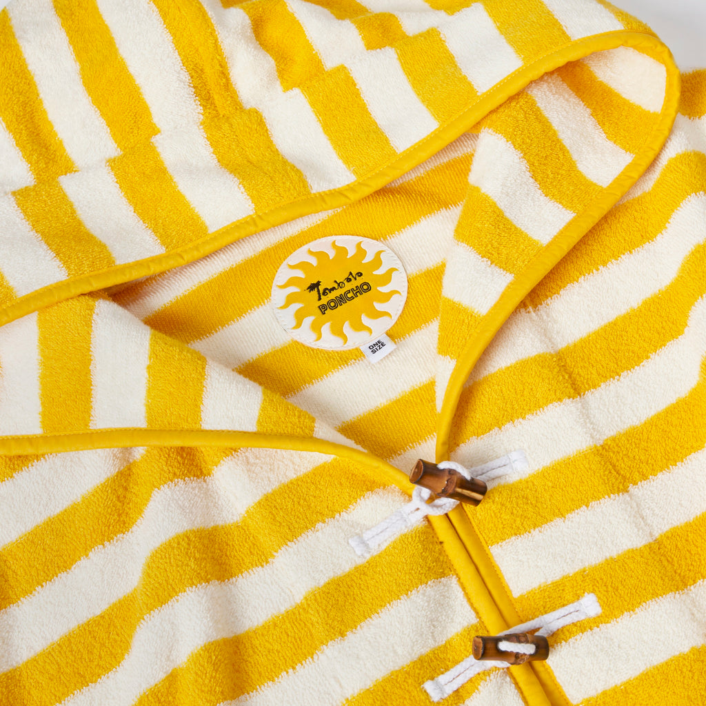 Close-up product image of the 'Saffron Stripe' beach towel top's circular interior tag with sun pattern and bamboo toggles and loop holds.