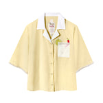 Light yellow short-sleeve button-up shirt with a white collar and pocket. The pocket has embroidered lime and chili pepper details. White beaded trim on the sleeves.