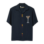 A navy blue short-sleeve button-down shirt with playful detailing: embroidered olive skewers act as buttons down the front, and a white martini glass with an olive garnish is embroidered on the chest. 