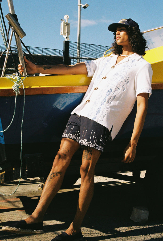 male model hanging onto pole on boat leaning back in marie de buttet shirt and fruits de mer navy shorts