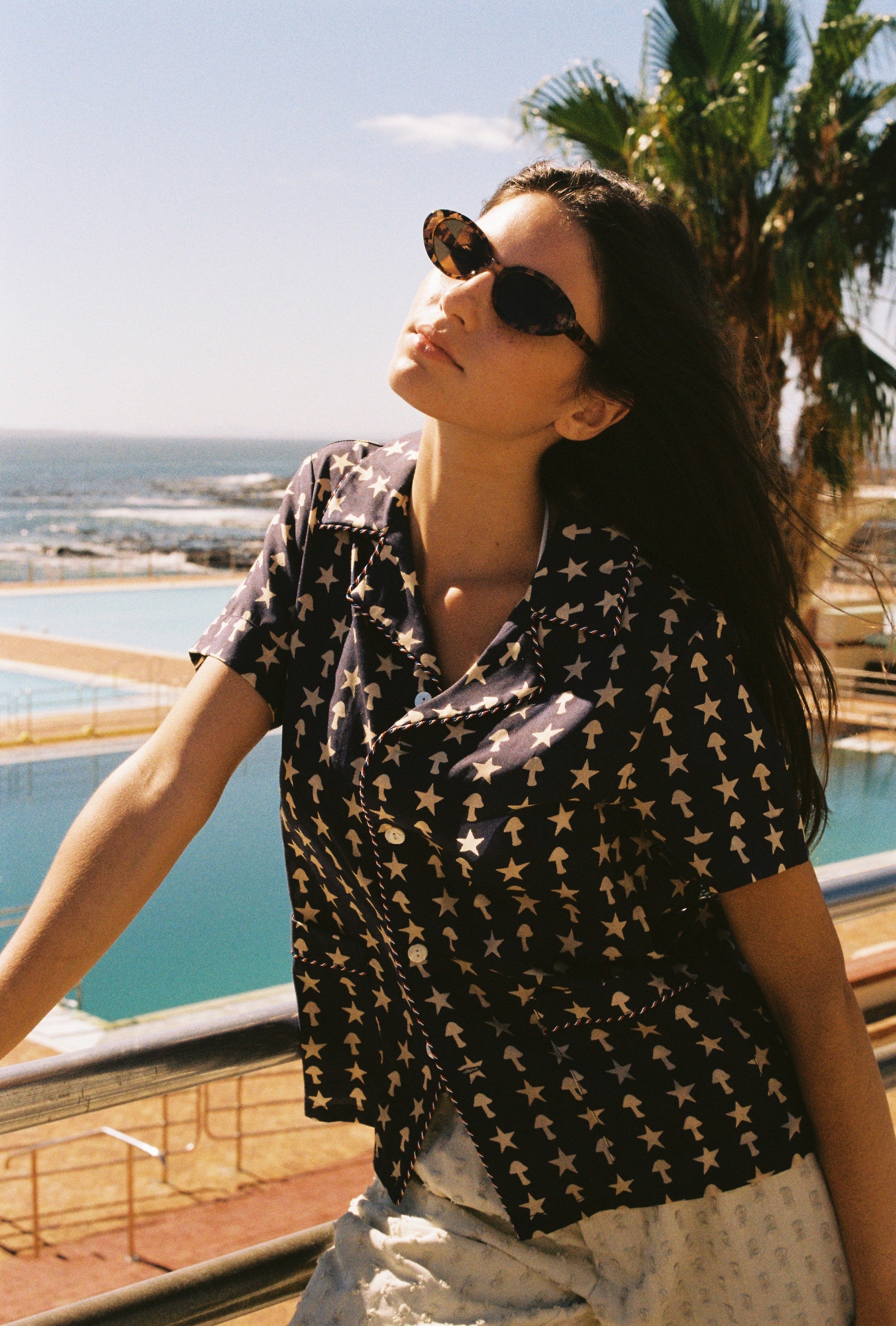 Female model posing in shirt with head tilted next to three pools