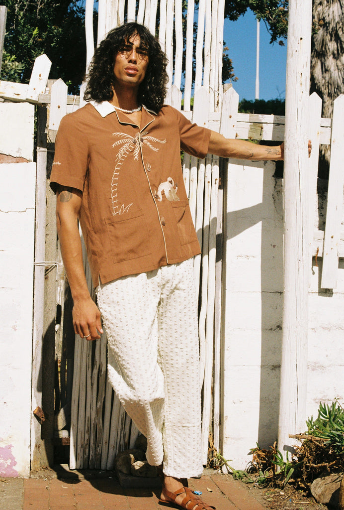 male model leaning while holding pole in our monkey business shirt with white pants