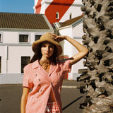 woman holds onto hat and looks at camera