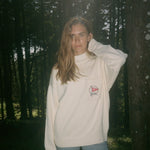 Woman in the woods looks off camera wearing Mariner sweater