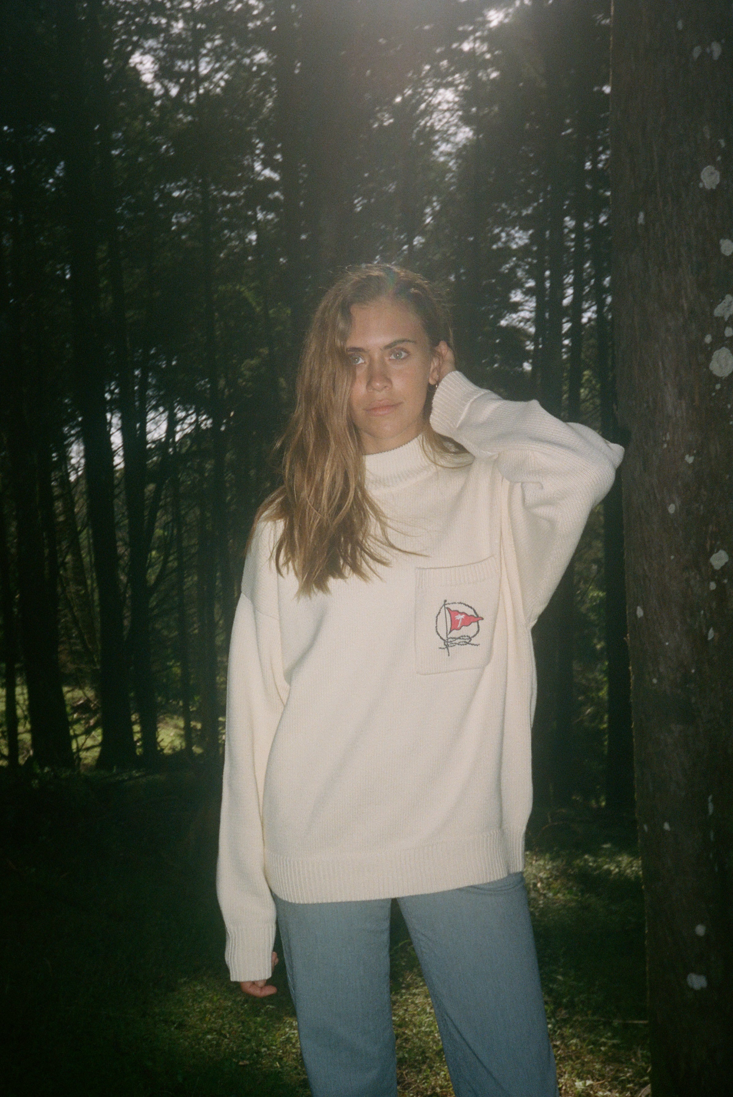 Woman in the woods looks off camera wearing Mariner sweater