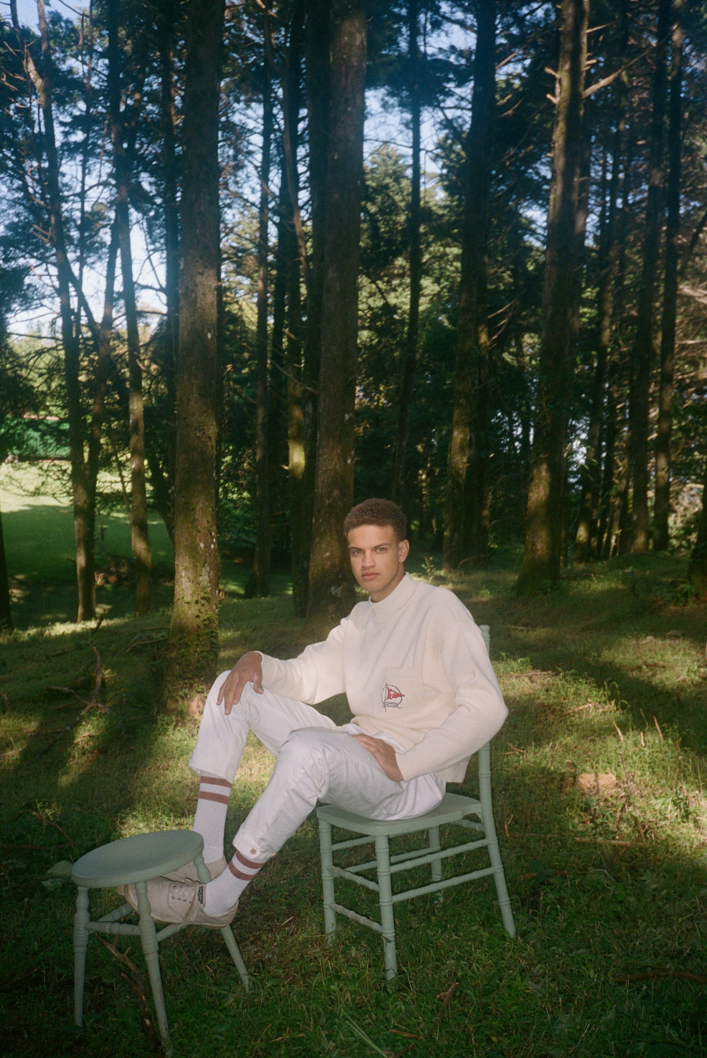 Man sits on chair with feet resting against a stool in the middle of forest
