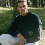 Man sits on stool in forest gazing at camera
