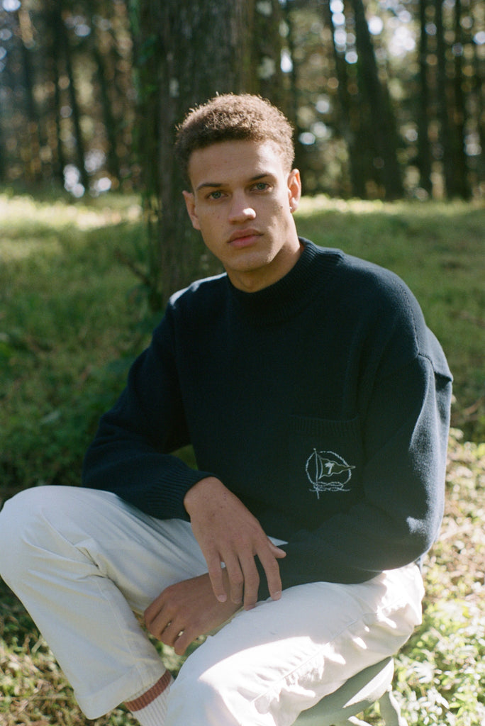 Man sits on stool in forest gazing at camera