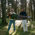 Younger man and older man in navy and beige sweaters hold woman lying horizontally across them