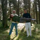 Younger man and older man in navy and beige sweaters hold woman lying horizontally across them