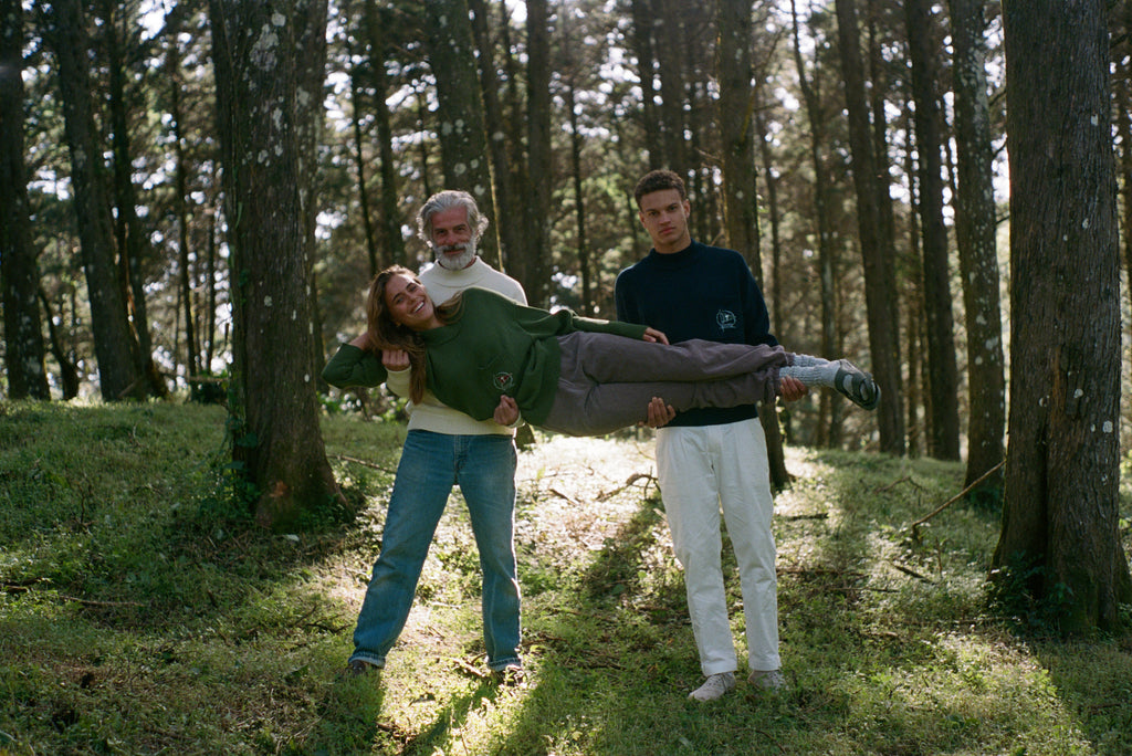 Younger man and older man in navy and beige sweaters hold woman lying horizontally across them